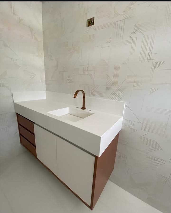 Lavabo com bancada e cuba esculpida em quartzo branco, sobre um gabinete com portas brancas e gavetas amadeiradas.