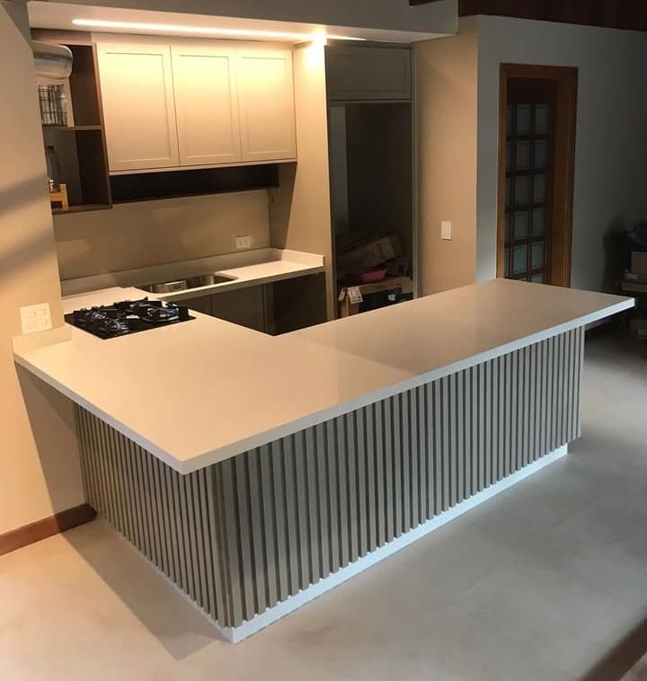 Cozinha com balcão em L com tampo branco e base com acabamento ripado em tom neutro.